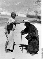 Near Lhasa. A pilgrim who measures the road with full body-length prostrations, stops to bless a woman.